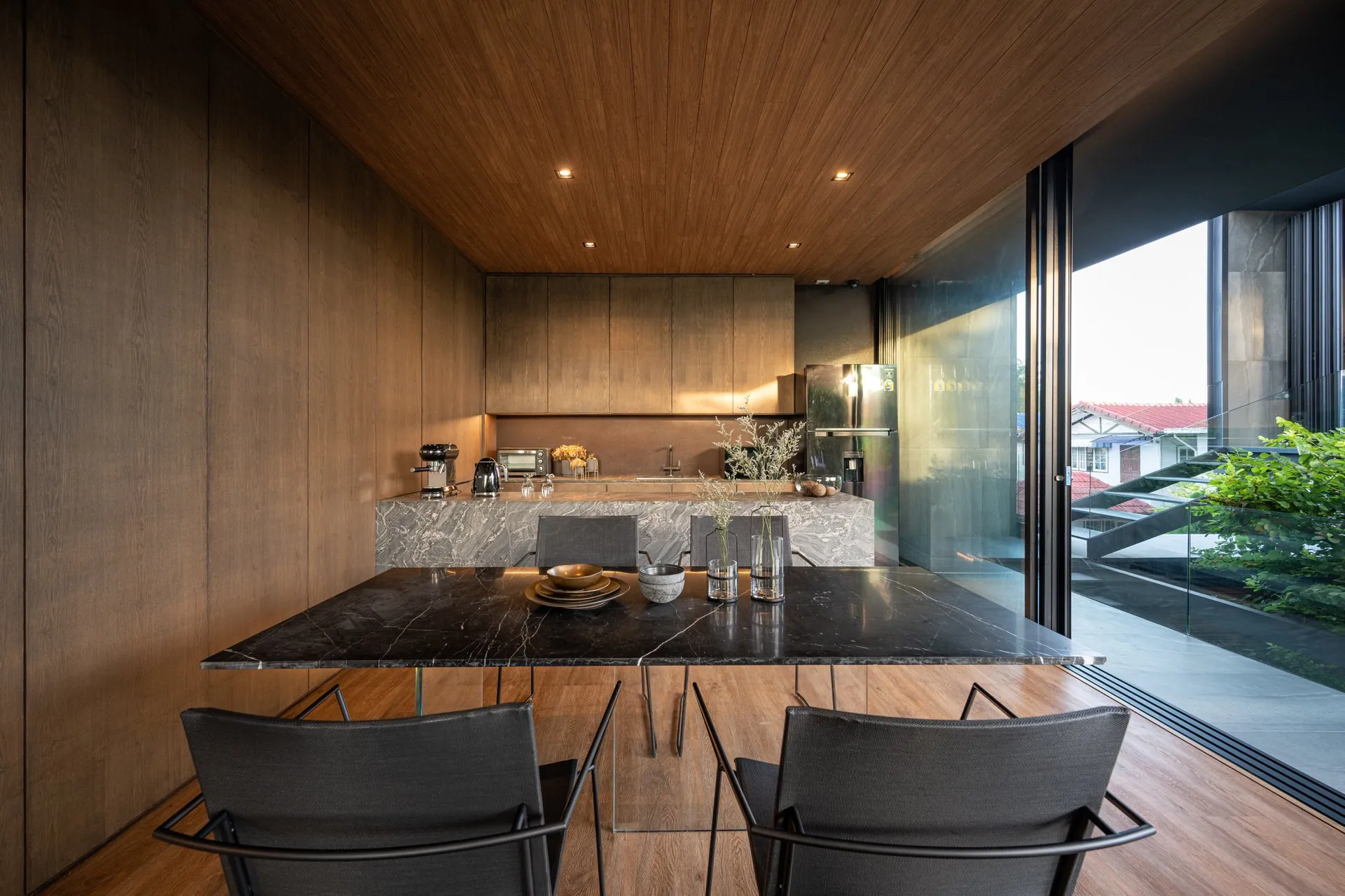 A modern residential kitchen featuring a marble countertop with stainless steel appliances and black chairs.