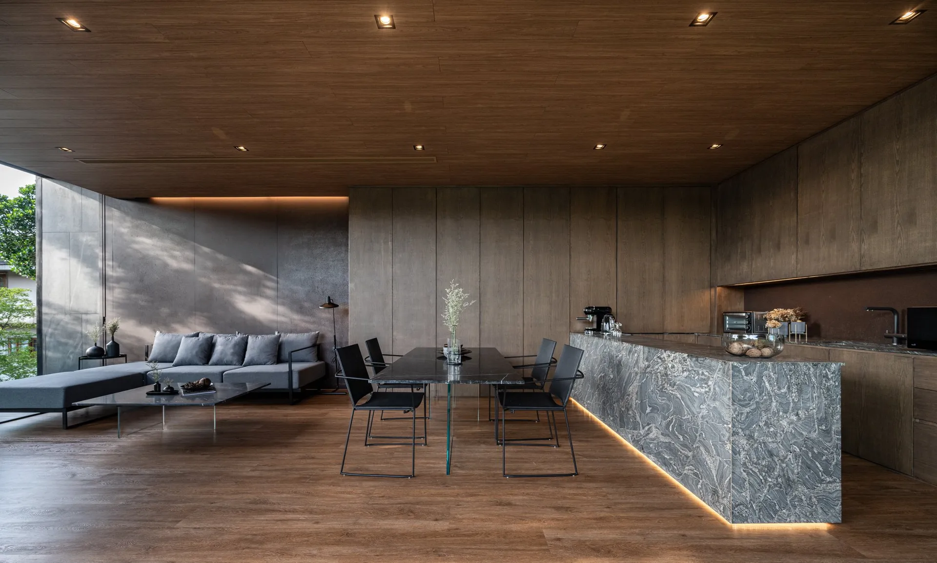 Modern living and dining area with a wooden ceiling and floor, featuring a grey sectional sofa, a black dining table with cha
