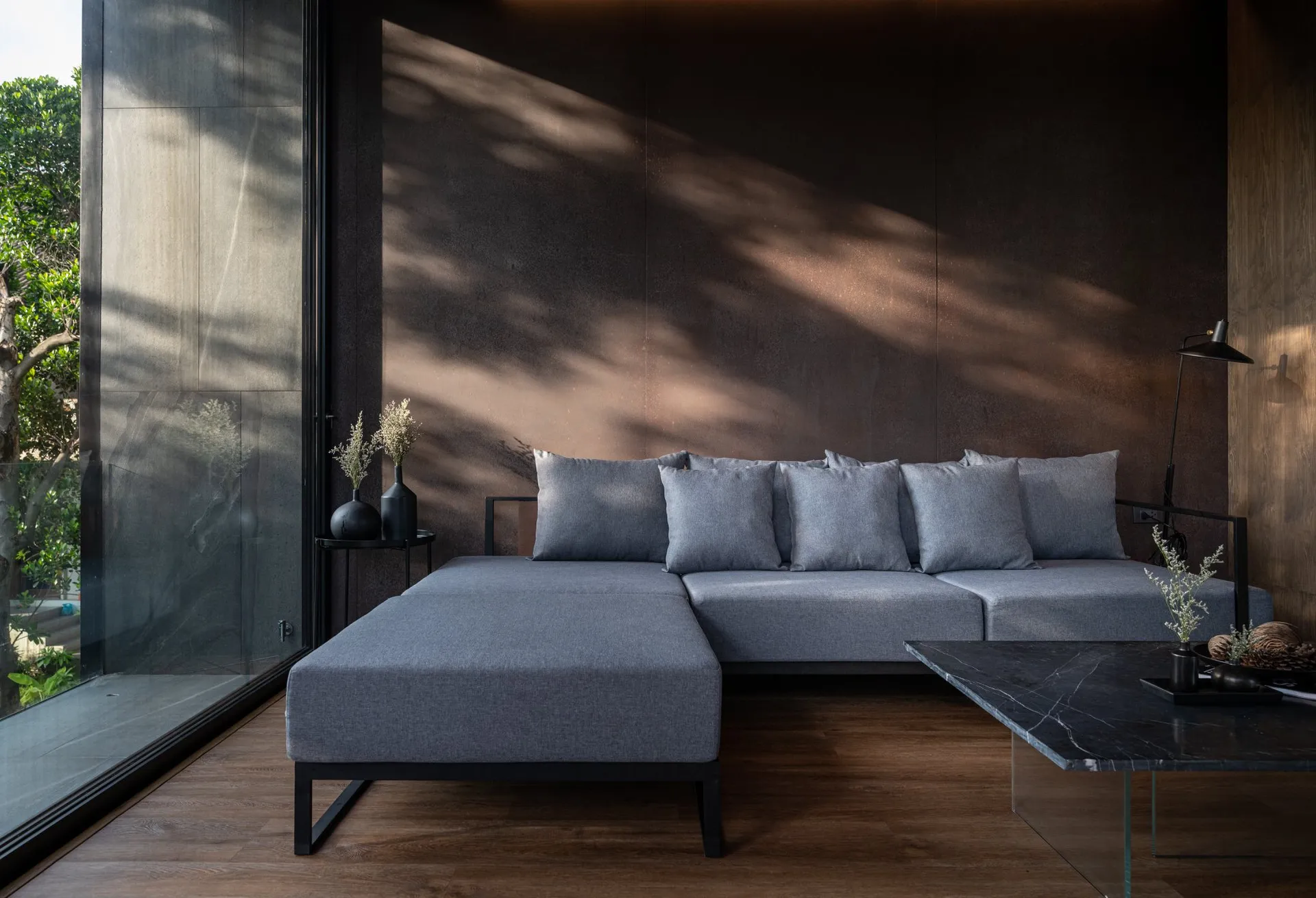A modern living room featuring concrete walls, a spacious grey sofa, and a sleek black coffee table.
