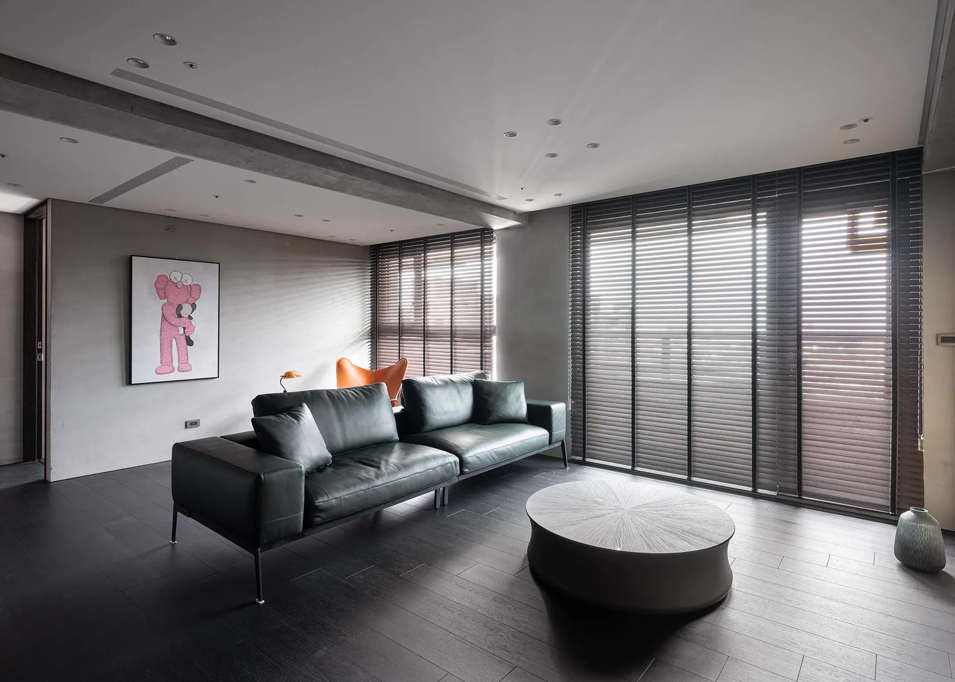 A modern living room with concrete walls, black leather sofas, and dark wood floors.