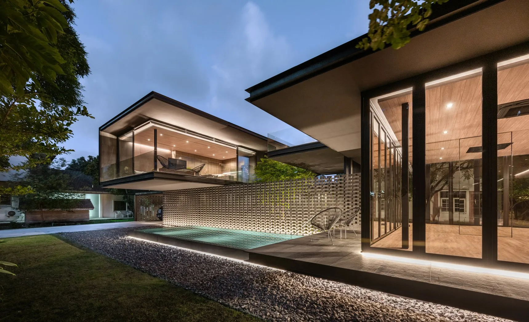 Modern minimalist house with glass walls and wood accents under a twilight sky.