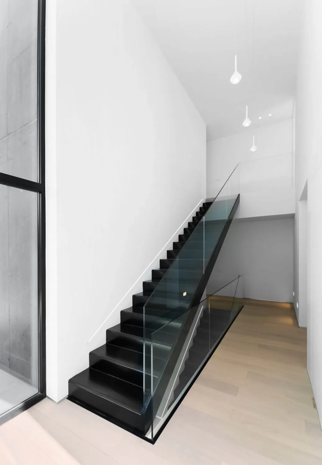 Staircase with black steps and glass railings in a minimalist interior setting.