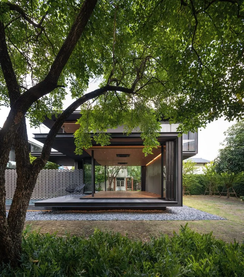 Modern house with glass walls and wooden deck surrounded by greenery.