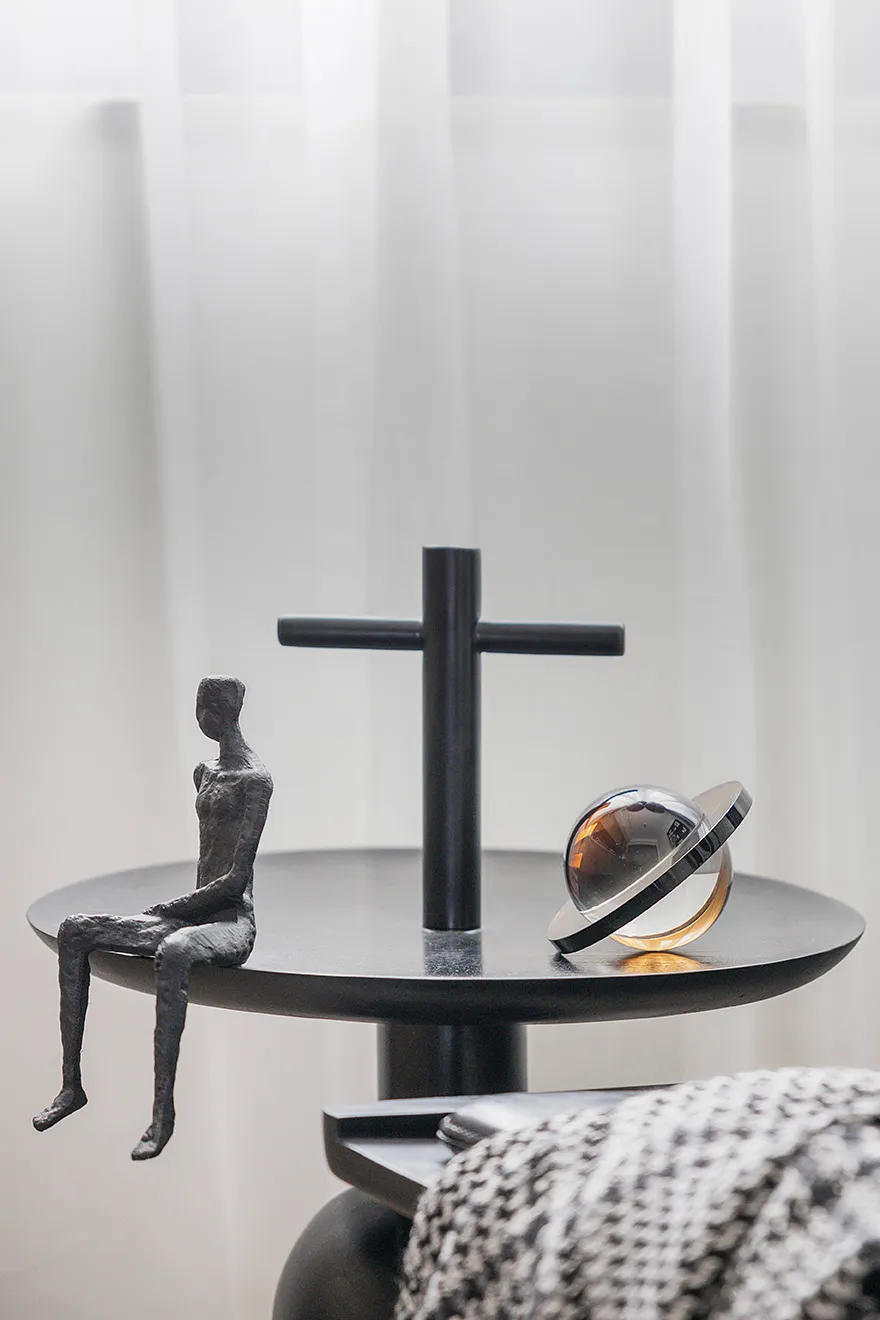 A minimalist interior design featuring a metallic shelf unit with abstract sculptures and a reflective globe.