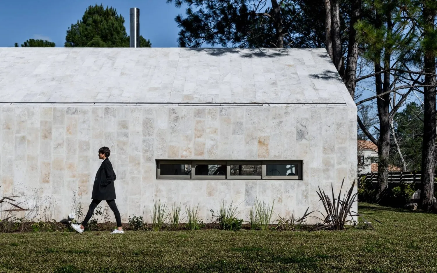 A woman walks past a modern architectural building with a stone exterior.