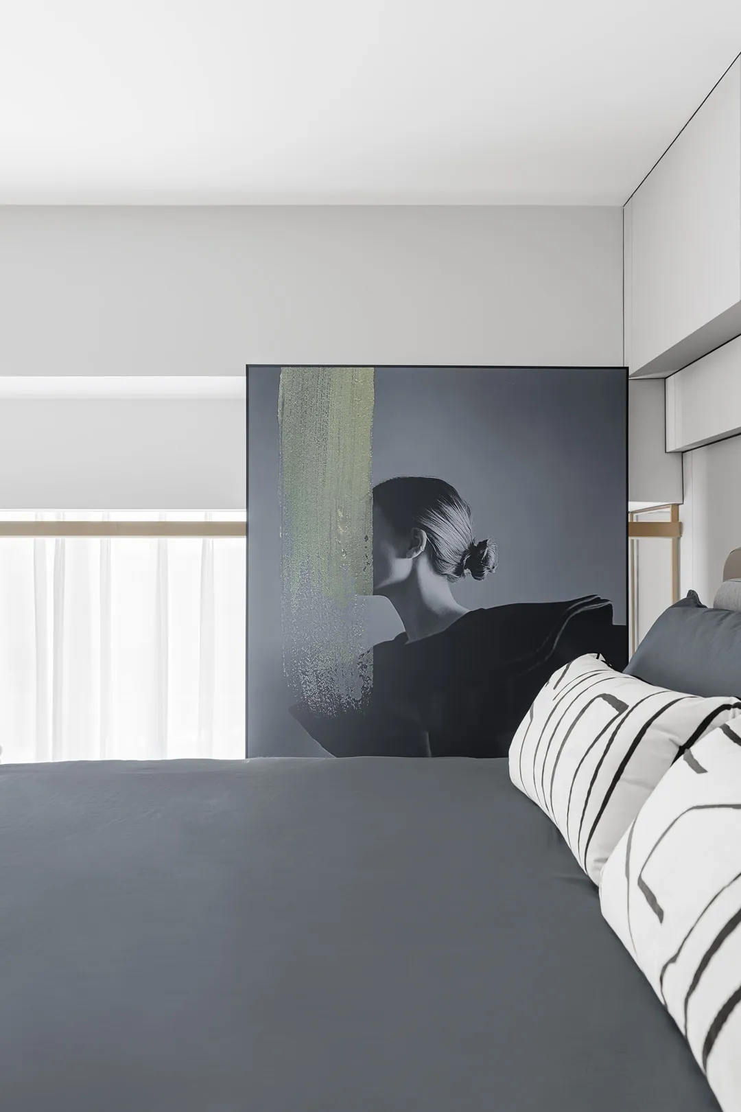 Modern minimalistic bedroom with gray bedspread and cushions, featuring a stylish wall art of a woman.
