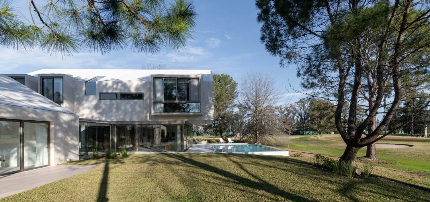 Modern residential home extension with a concrete facade, large glass windows, and a swimming pool in the garden.