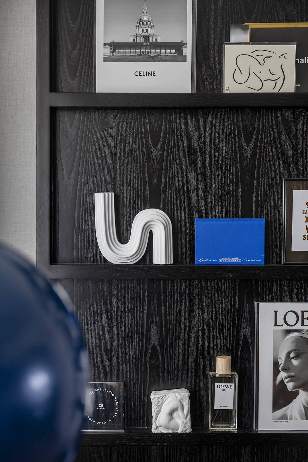 A modern black shelf with a combination of wood and concrete textures, displaying various decorative items including a Celine