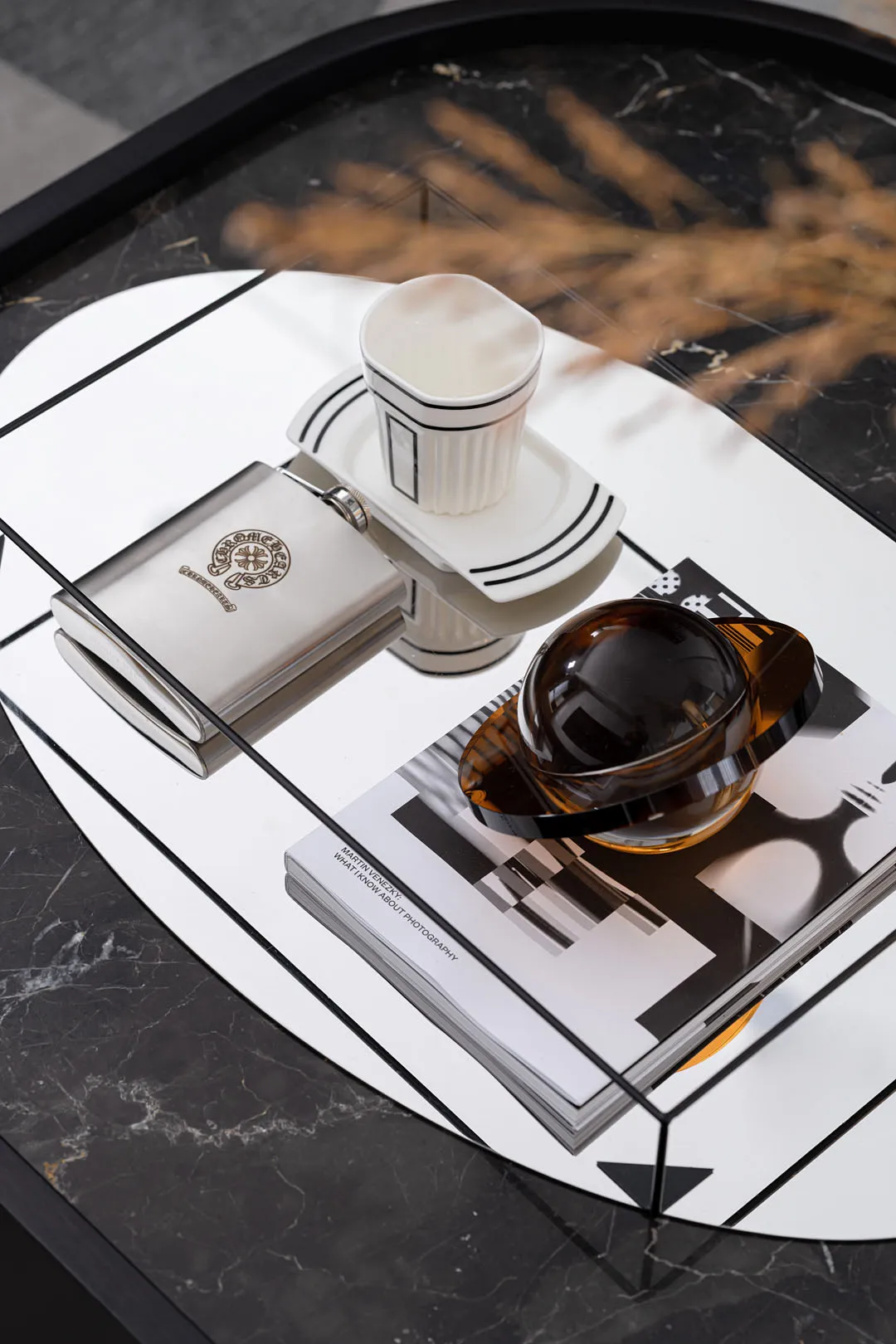 Minimalist coffee table with a white marble surface and various items such as a hip flask, a ceramic cup, a teapot, and a boo