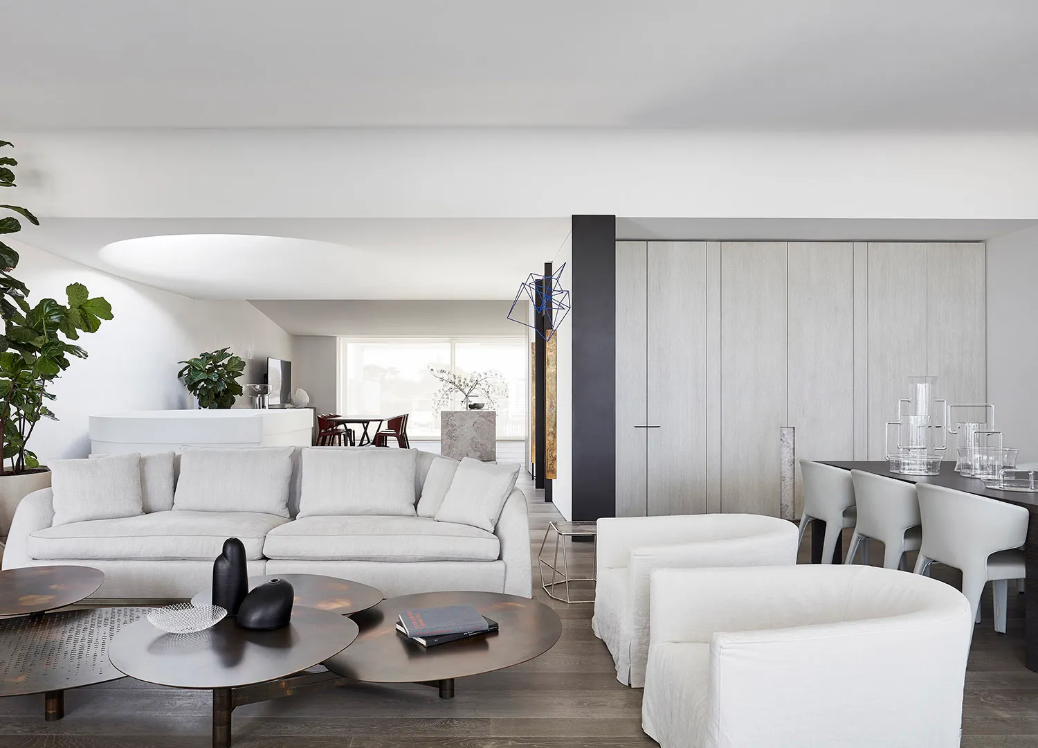 A minimalist living room featuring sleek, white furniture and wooden flooring.