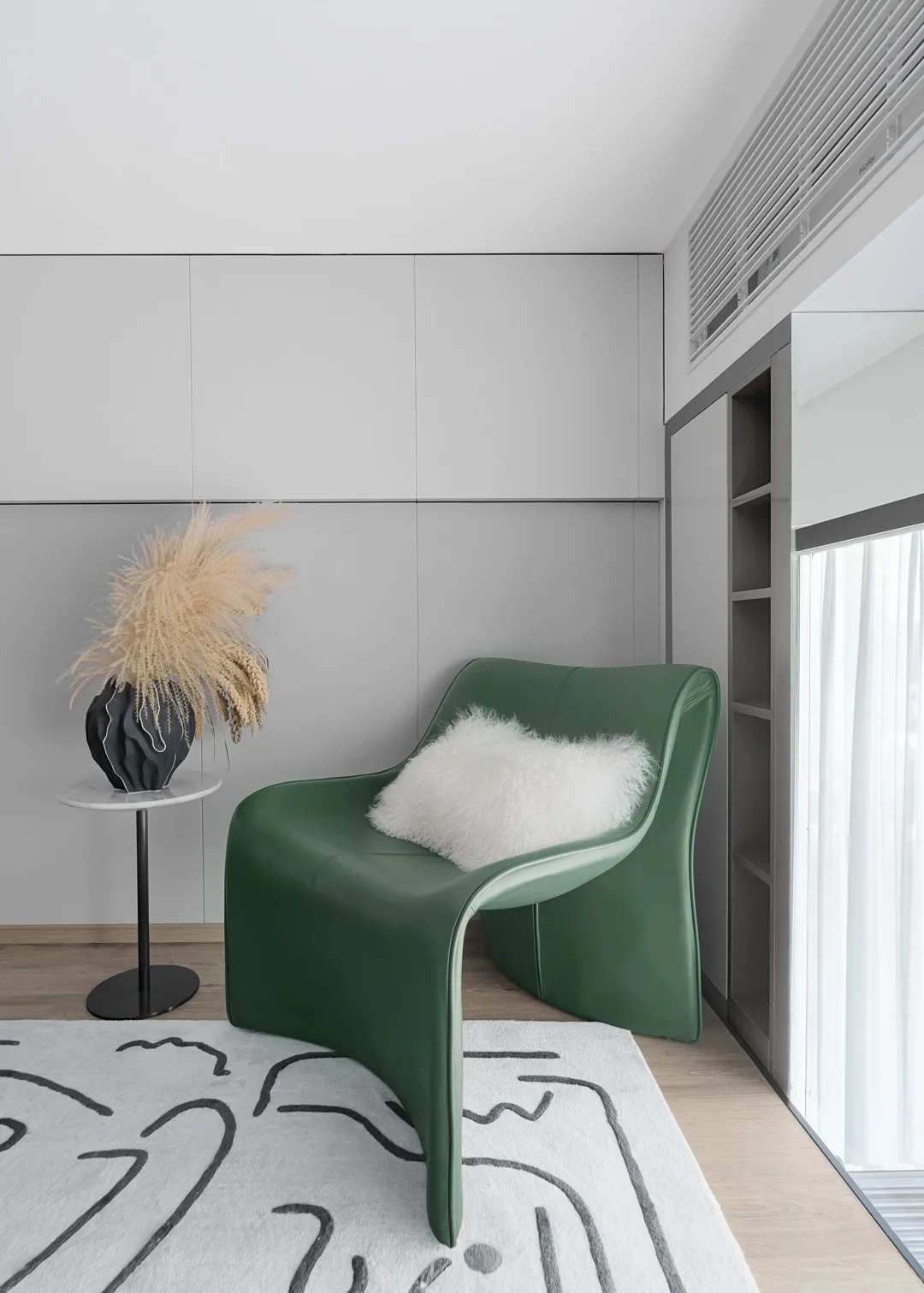 Modern living room featuring a green leather chair with a fluffy white pillow, styled with dried grass flowers in a vase on a