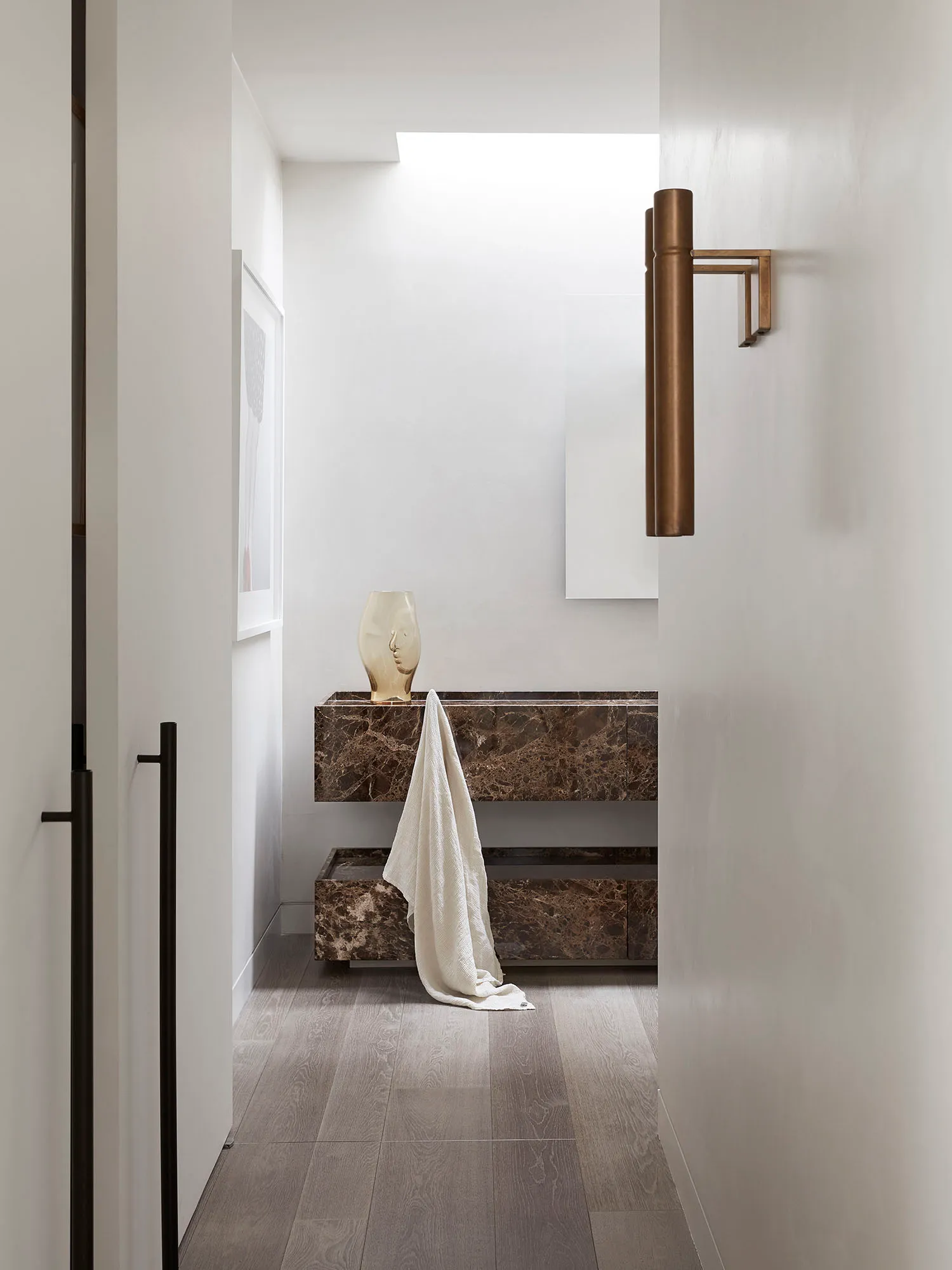 A modern marble bathroom with a minimalist design featuring a vase on a counter and a towel draped over the edge.