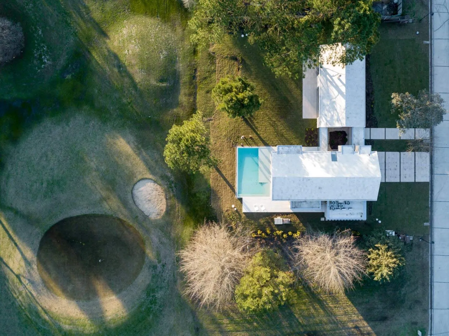 A modern house with a concrete exterior and a pool surrounded by greenery.