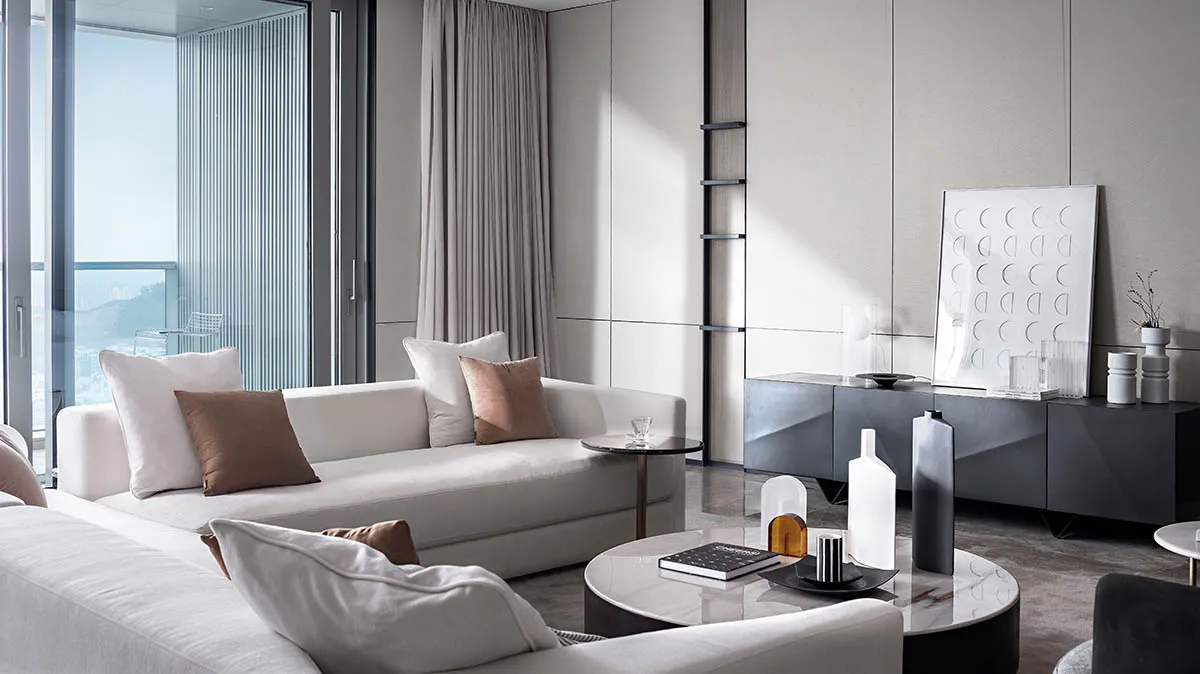 A modern living room featuring white sofas with brown and beige cushions, glass coffee tables, concrete accents, and large wi
