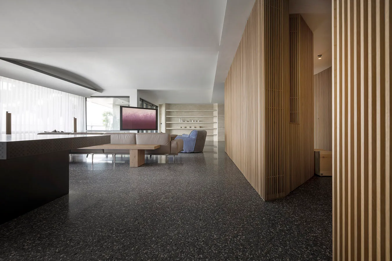 Modern living room featuring a couch, table, and minimalist decor with wood, glass, and concrete materials.
