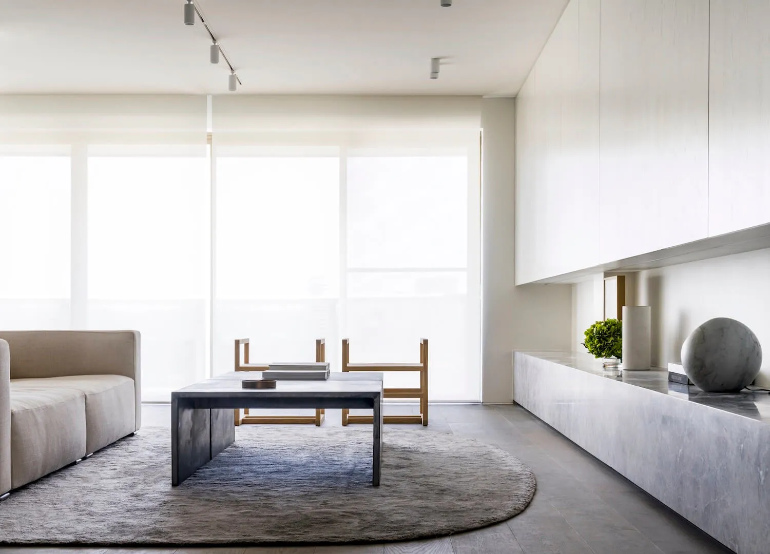 Modern living room featuring a concrete coffee table, minimalist furniture, and large windows.