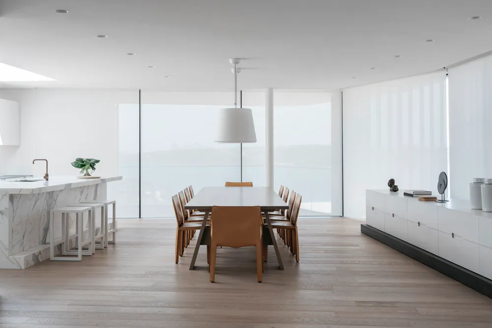 A modern, minimalist space featuring a minimalist dining table with white marble top, surrounded by white chairs in a light-f