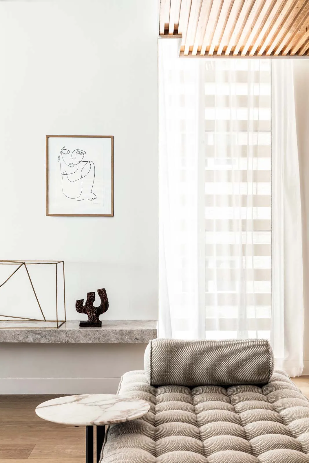 Modern residential living space with concrete walls, sheer curtains, marble coffee table, and grey tufted sofa