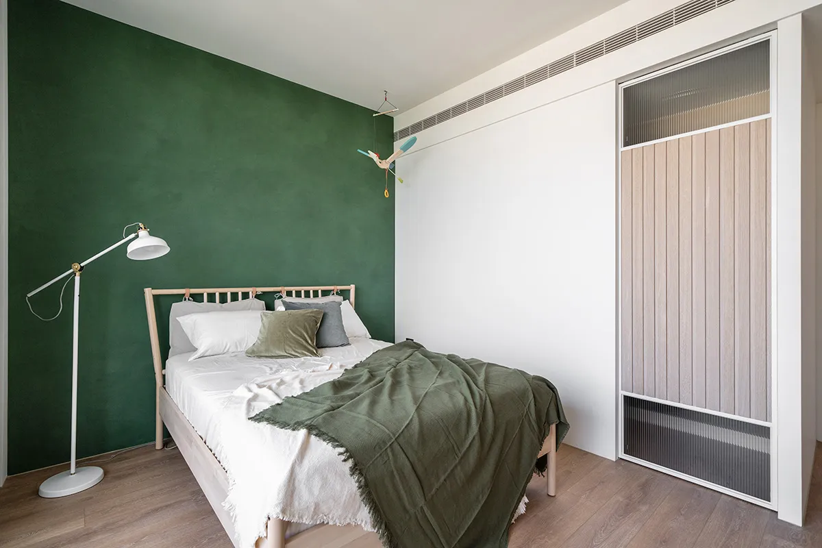 Modern, minimalist bedroom featuring a green accent wall, white bedding, and a wooden bed frame.