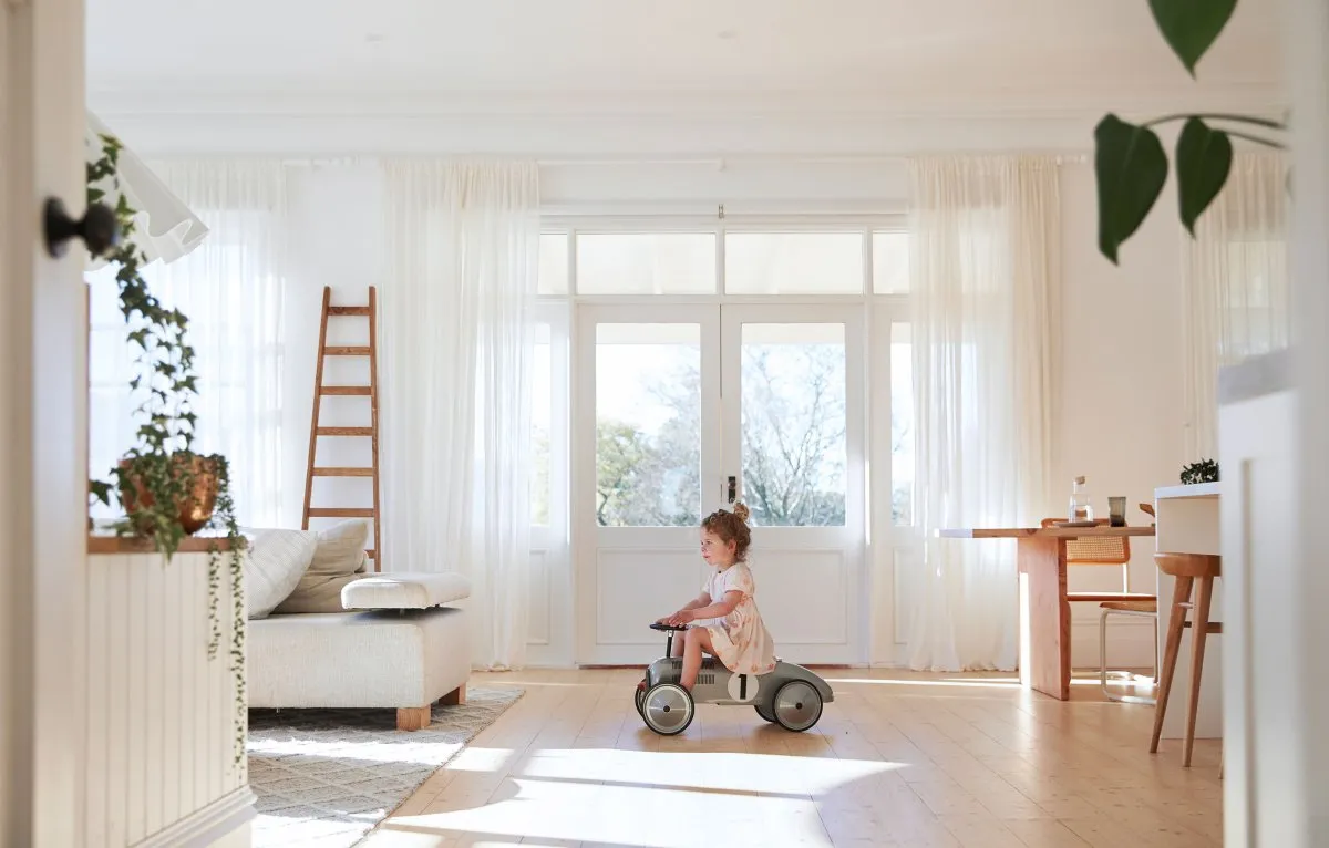 A minimalist living room featuring white window curtains, hardwood floors, and a wooden ladder.