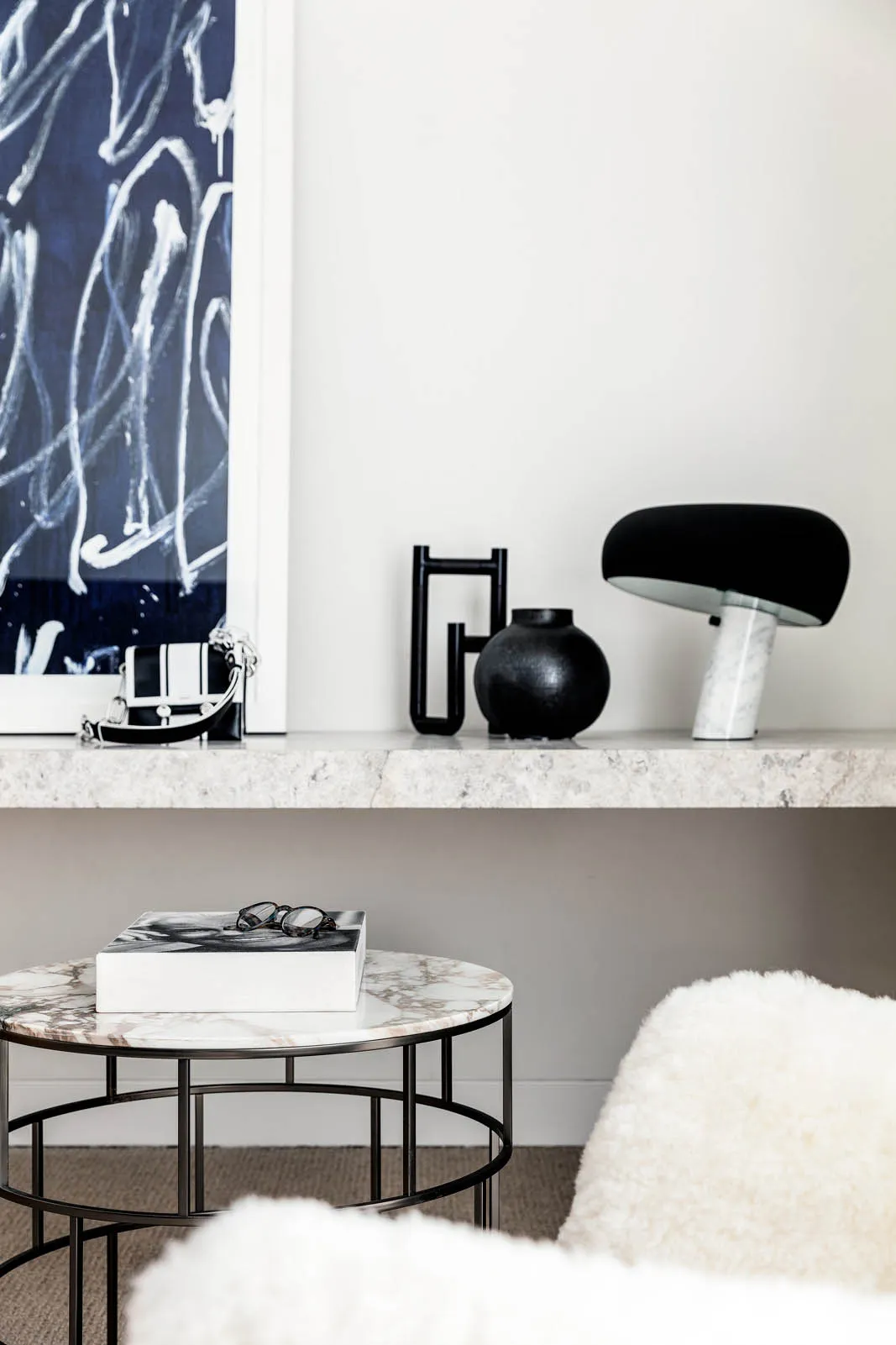 A modern, minimalist setting with a round marble side table featuring a metal frame, accompanied by a black and white abstrac