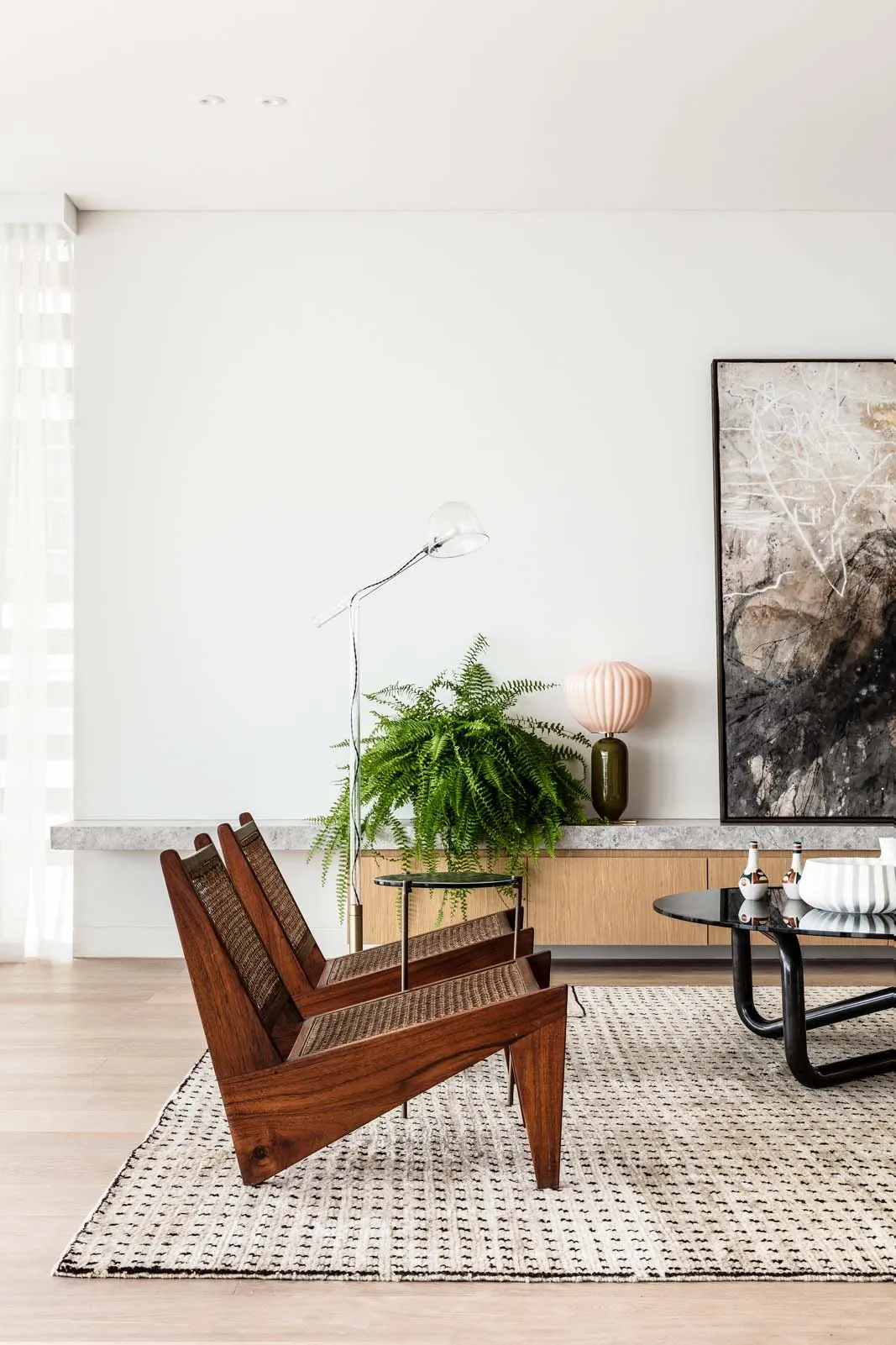 A modern living room featuring wooden furniture, a large potted plant, and a abstract painting.
