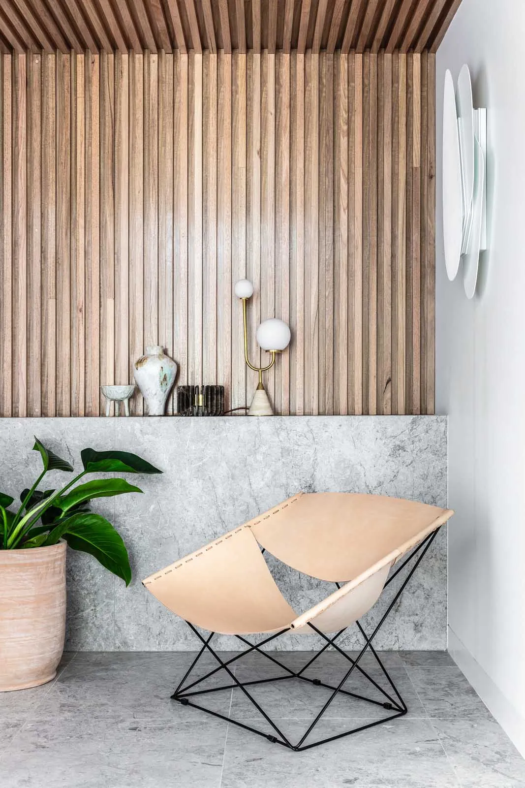 A modern living space featuring a wooden wall and grey concrete floor, with a unique leather chair and a potted plant.