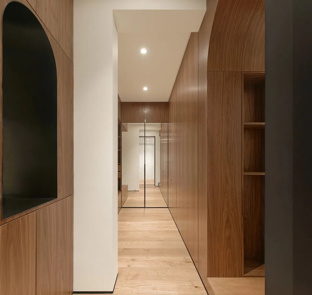 A minimalist corridor with wooden walls and flooring, featuring arches and recessed lighting.