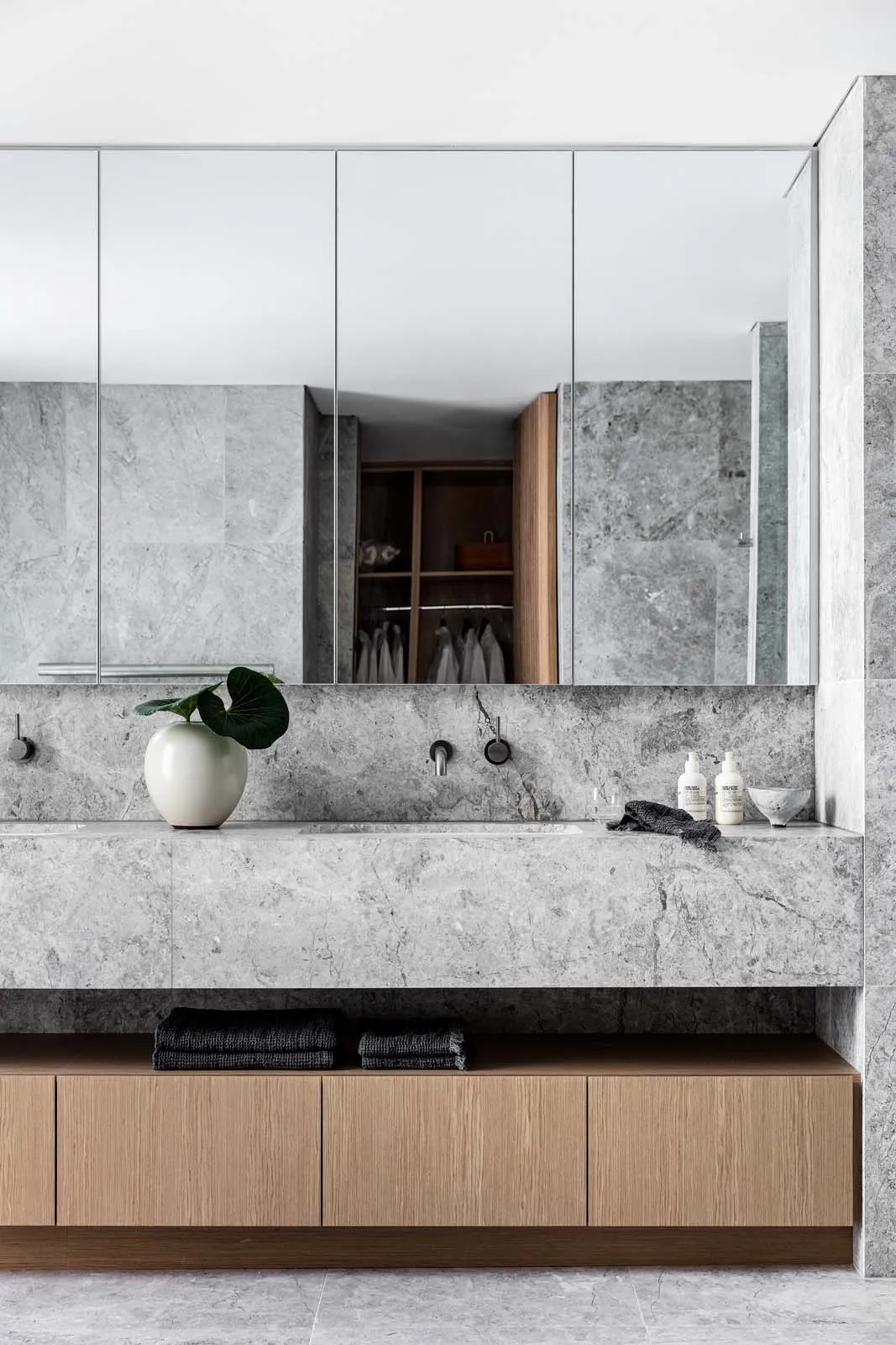 Modern bathroom featuring marble tiles and countertops, with a wooden vanity and minimalist design.