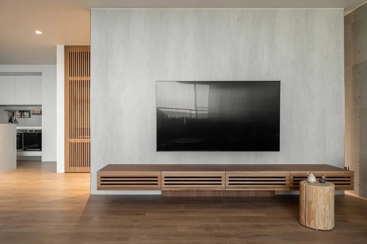 A modern living room features a wooden console table with concrete accents and a large television mounted on the wall.