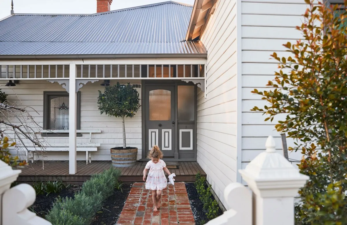 A white Victorian-style house with a grey roof, wooden siding, and brick walkway.