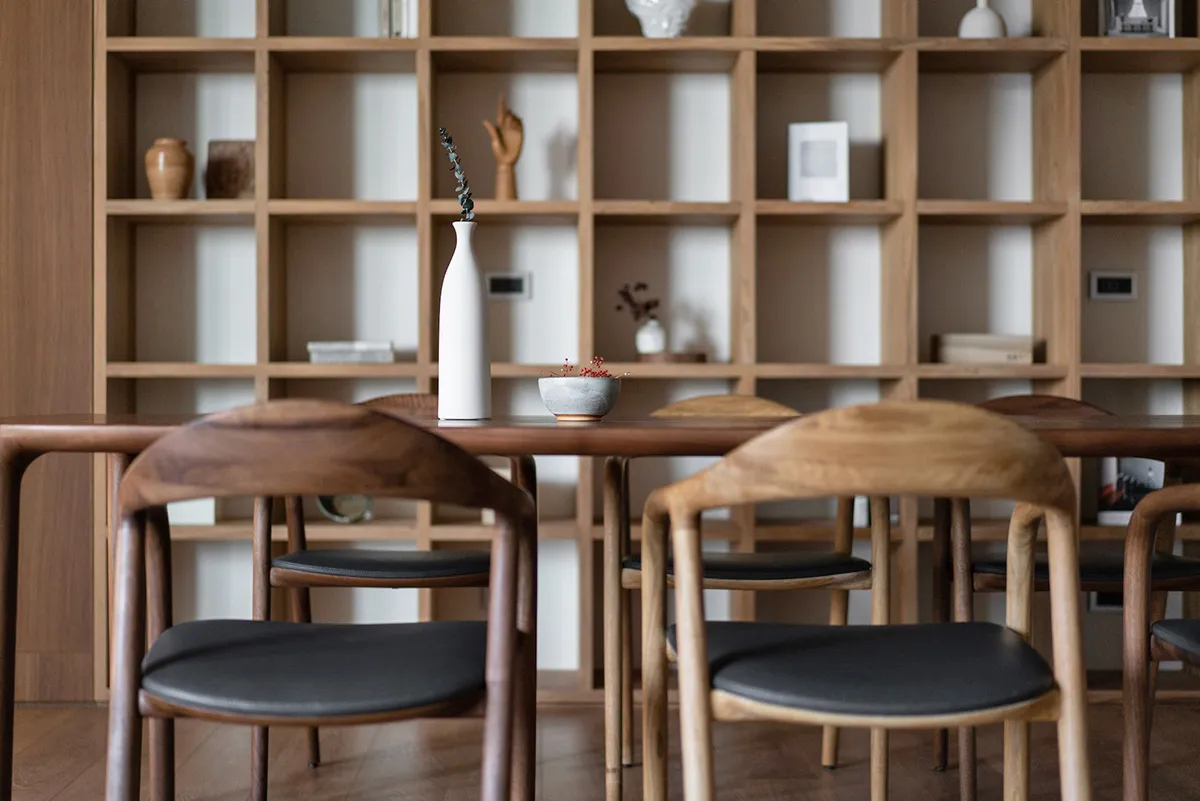 A minimalist dining room featuring wooden furniture, leather seating, and ceramic accents.