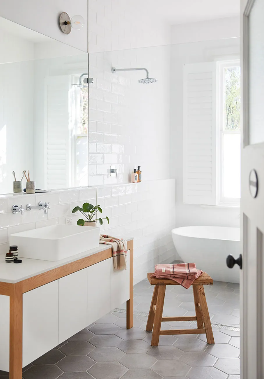 Modern bathroom interior with a white ceramic tile wall, a freestanding wooden vanity with a white countertop, and a grey hex