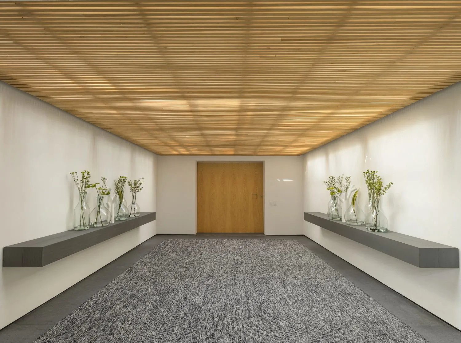 Minimalist lobby with concrete walls, wood ceiling, and glass vases.