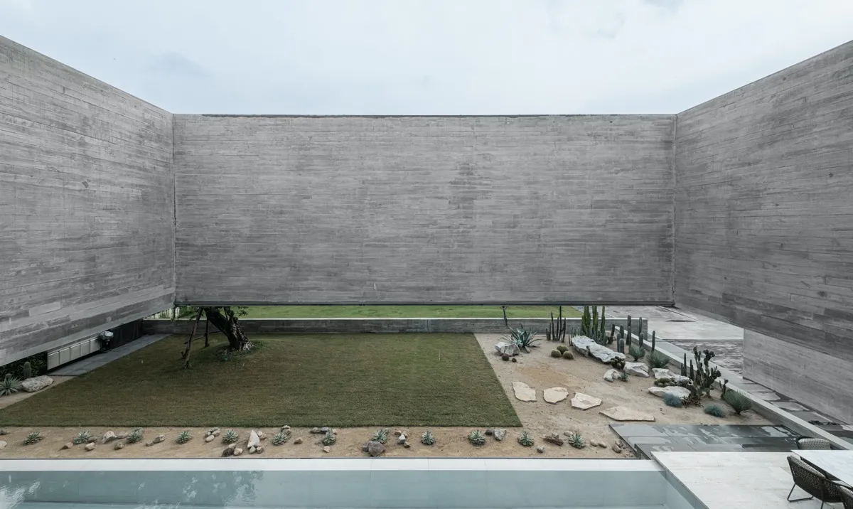 A modern outdoor space with concrete walls, a grassy area, and a small garden.