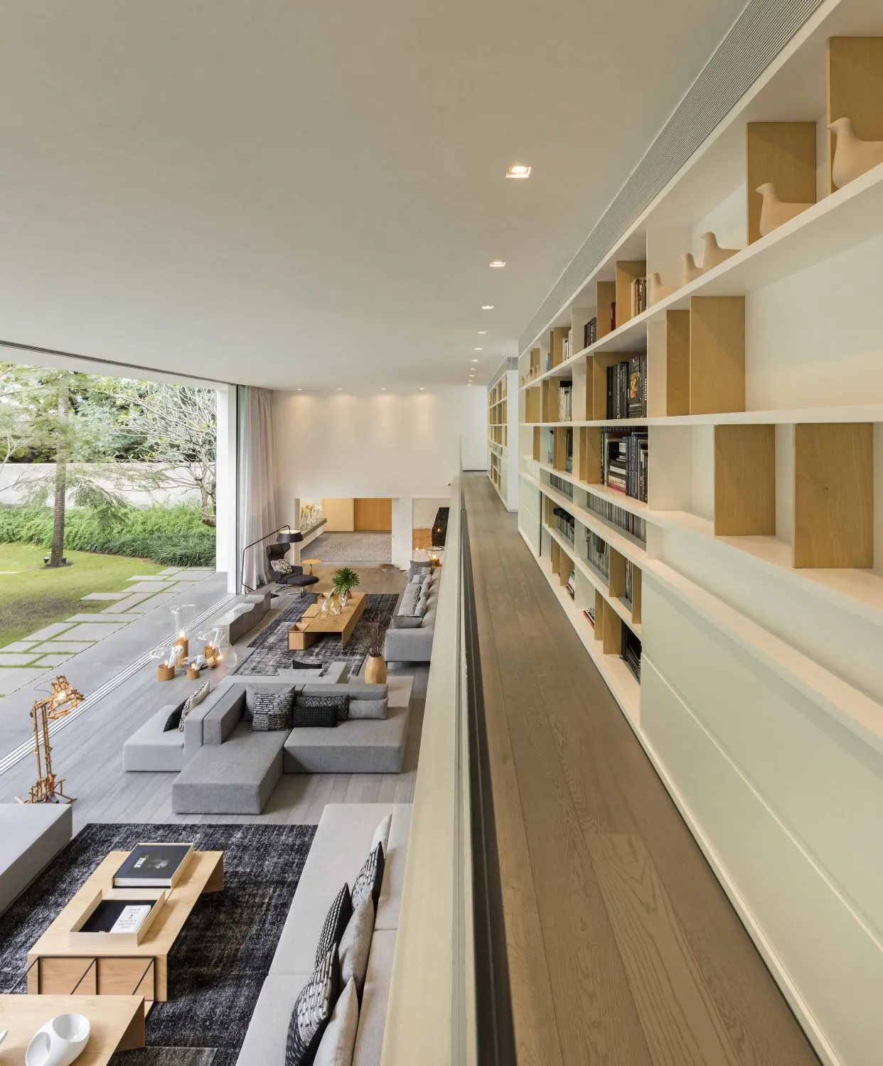 Modern living room with a long bookshelf filled with books and decorative objects, featuring light-colored wood flooring and