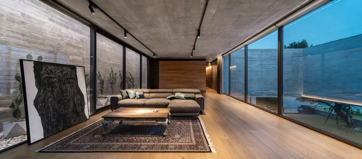 Modern living room featuring a concrete wall, wood floor, and large windows.