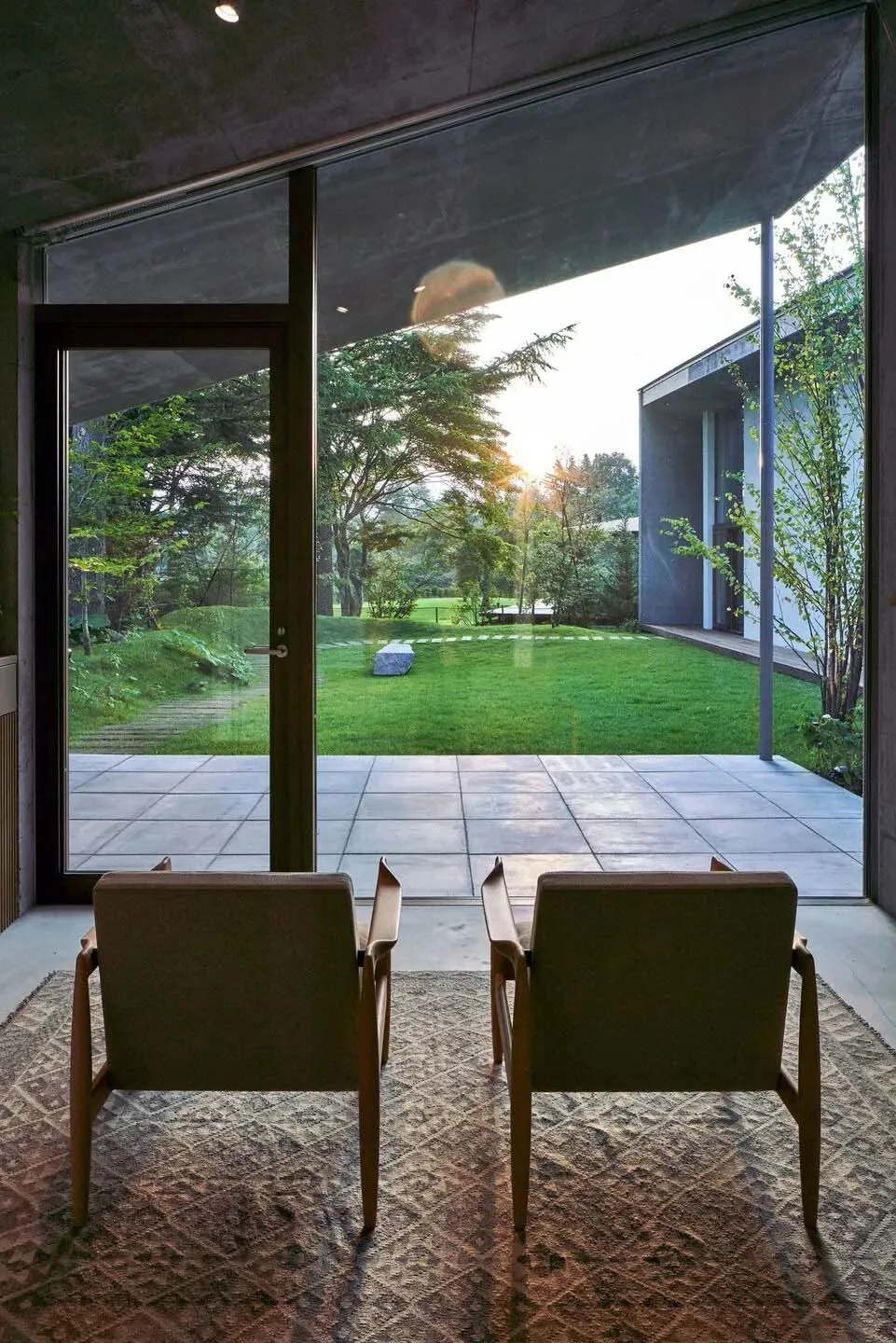 A modern living room with tile flooring, featuring two upholstered chairs and a patterned rug.