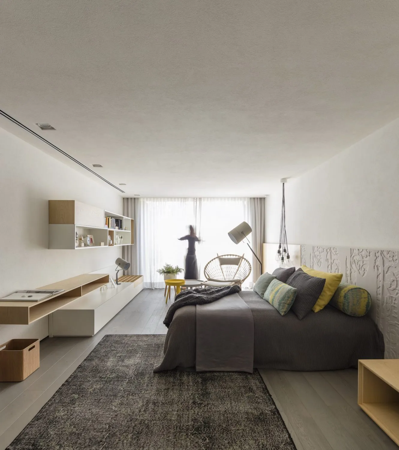 Modern minimalist bedroom with a bed, lamp, and chair near a large window.