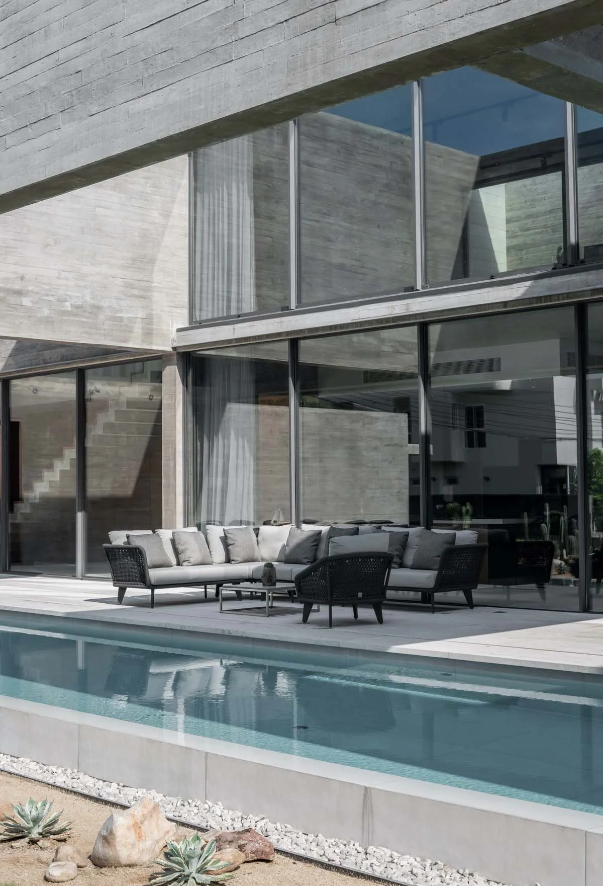 Modern minimalist landscape featuring concrete poolside seating and large glass windows.