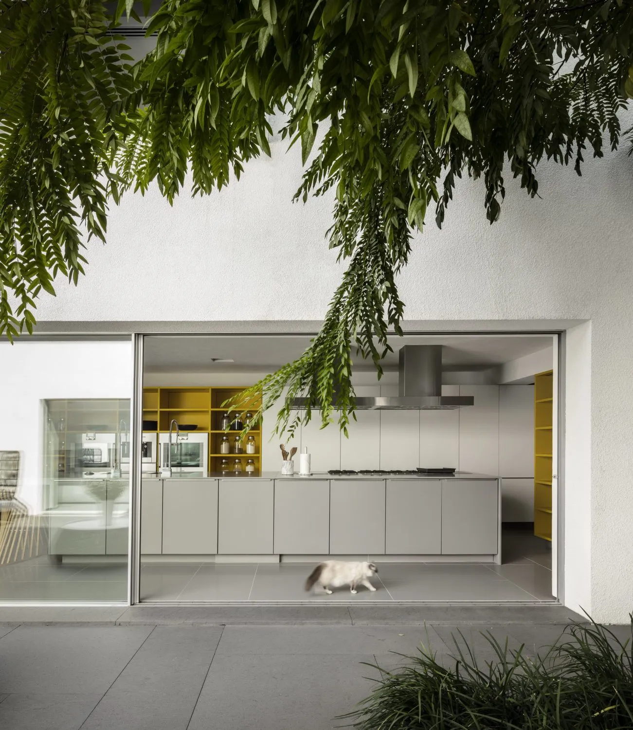 A modern minimalist kitchen with a white color scheme and yellow accents, featuring white cabinets, a white countertop, and a