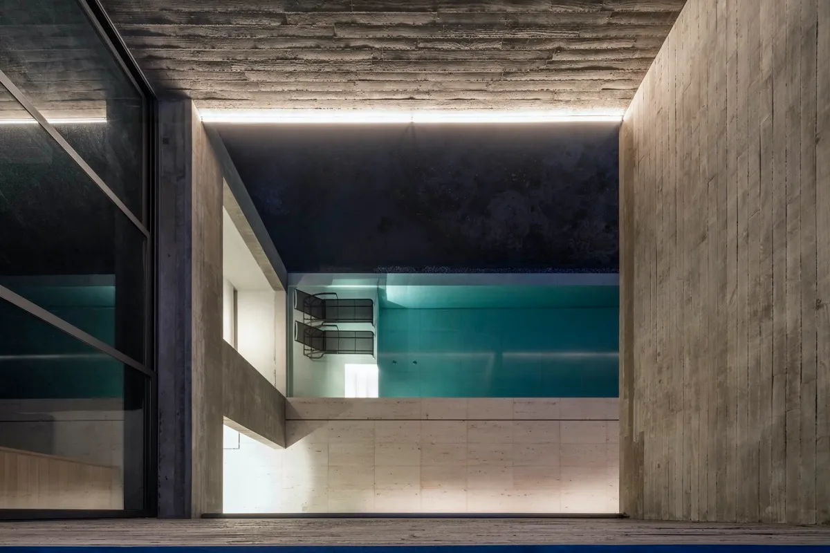 Modern minimalist swimming pool interior with concrete walls and floor, illuminated by recessed lighting.