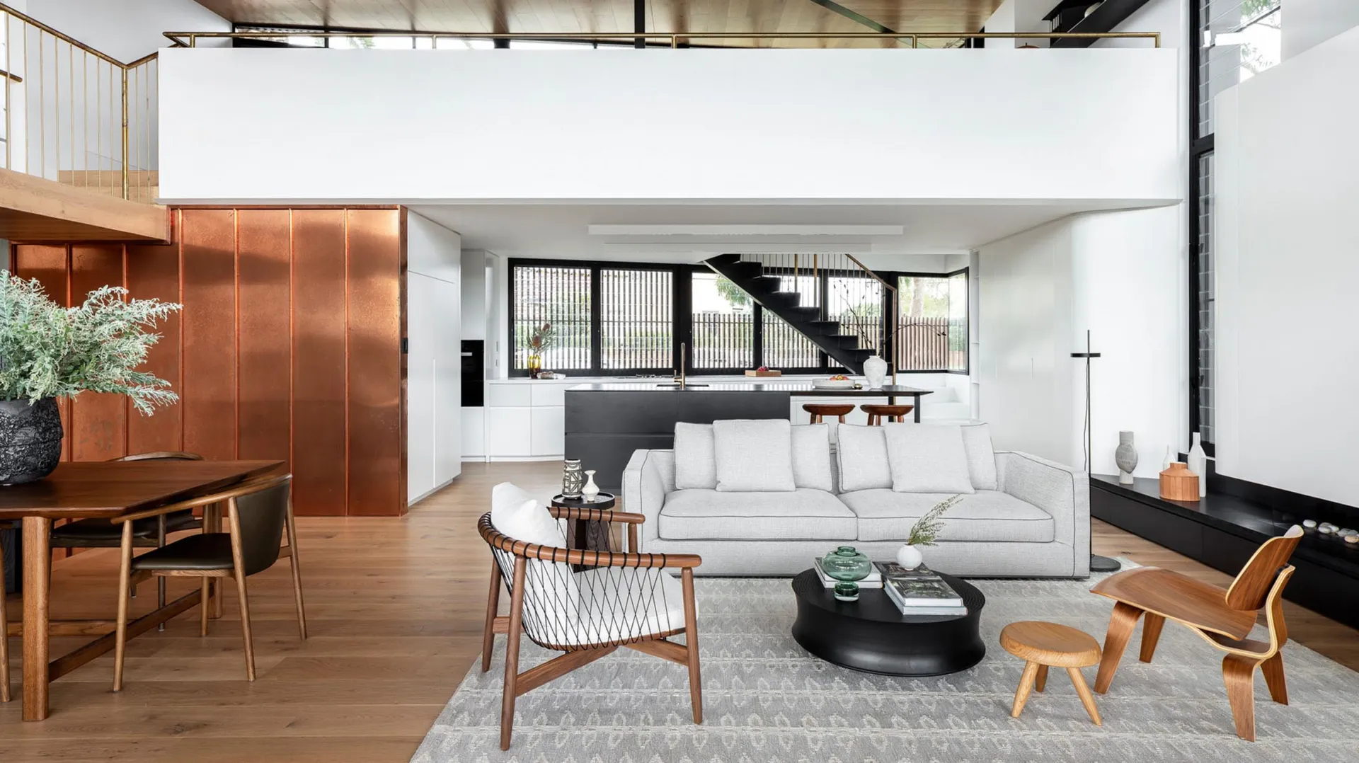 Modern, minimalist living room with white open-plan design, featuring a grey sofa, black and wooden furniture, and a grey rug