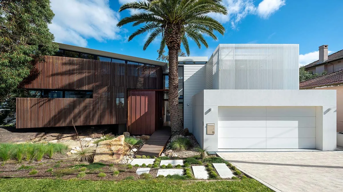 Modern residential house with wooden and metallic exterior, surrounded by greenery and palm trees.