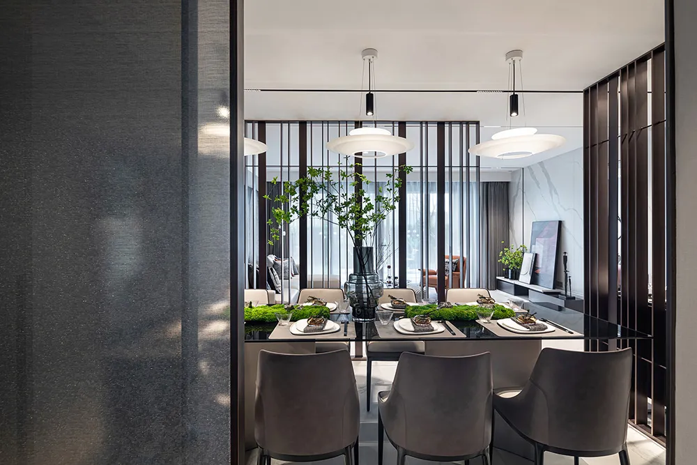 A modern dining room featuring metal, glass, and wood materials, with a long dining table set for a meal.
