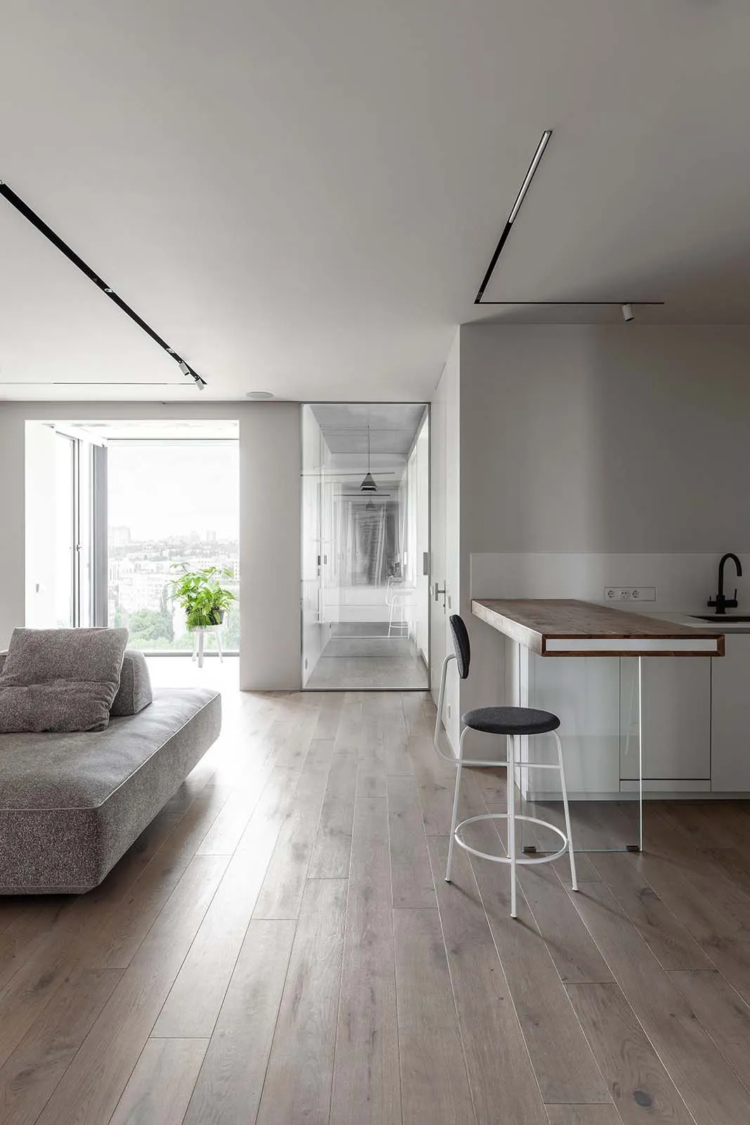A modern living space featuring wooden flooring, glass partitions, and metallic elements.