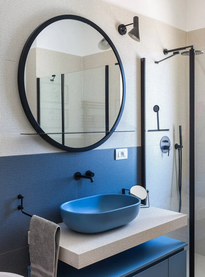 Modern minimalist bathroom with blue tiles, a blue ceramic sink, and a round black-framed mirror.