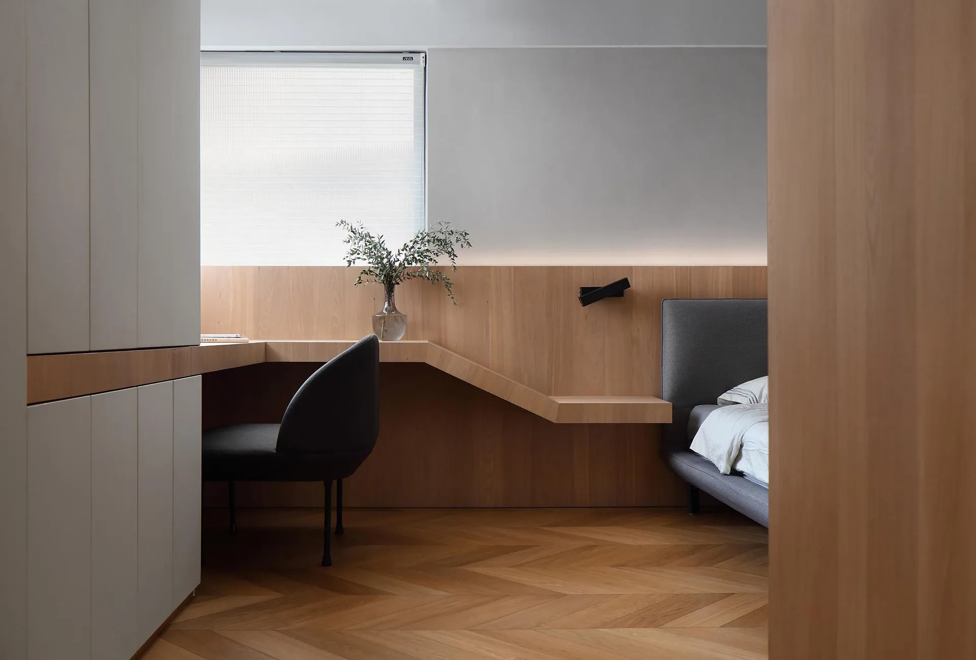 A minimalist bedroom with a wooden headboard and built-in desk area.