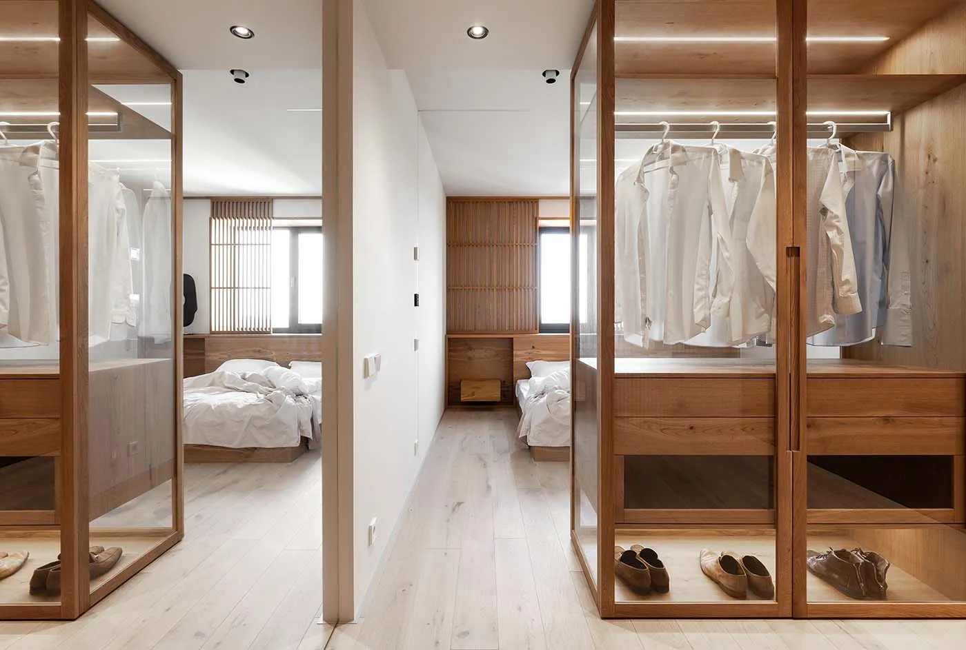 A modern minimalist bedroom featuring a large wooden closet with clothes hanging.