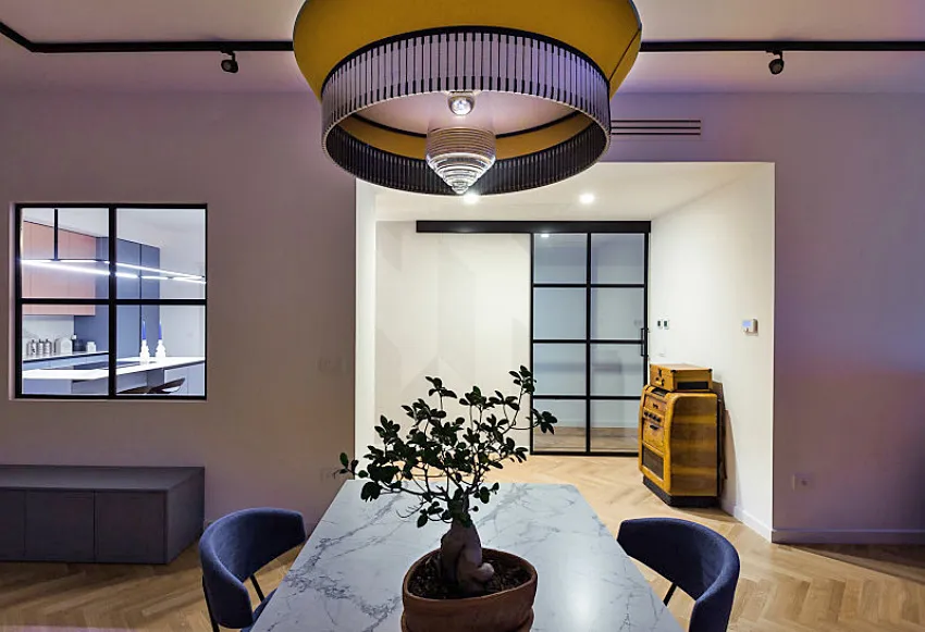 A modern dining room featuring a marble table with a bonsai plant, blue chairs, and a minimalist design.